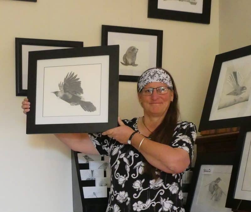 Tricia Hewlett holding up a Tui Artwork in her Studio